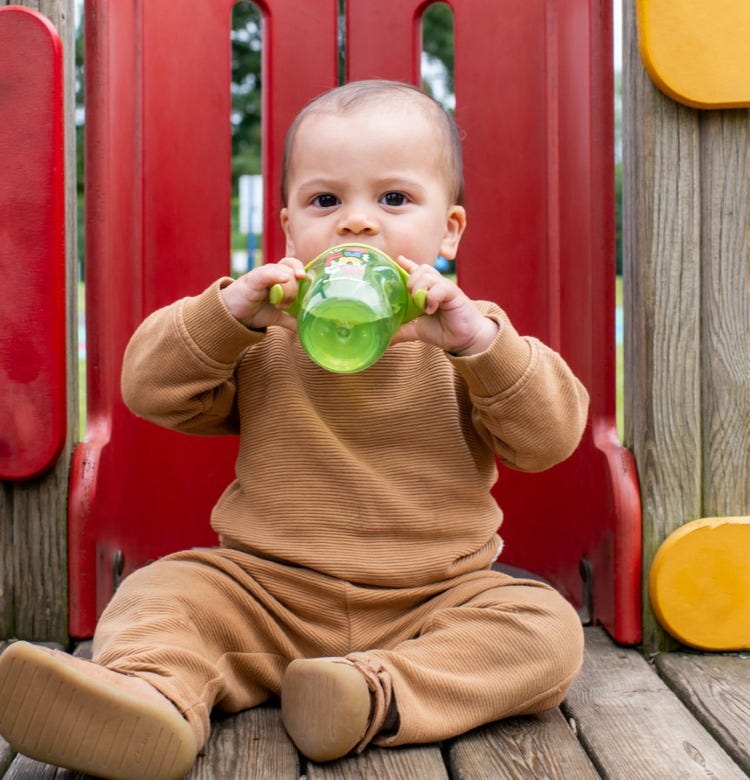When Your Baby Should Start Drinking Water toddler drinks from a cup in the park