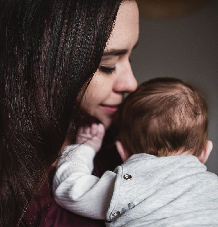 Our Guide to Baby Sleep Aids mom holding her baby who is wearing a grey sleep bag