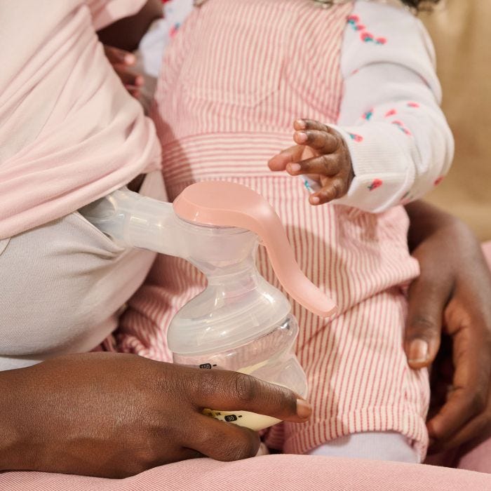 Parent manually expressing while holding baby.