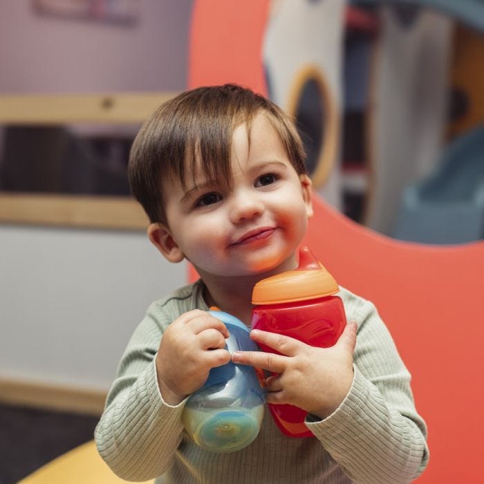 Toddler holding a blue and red sippee cup while smiling