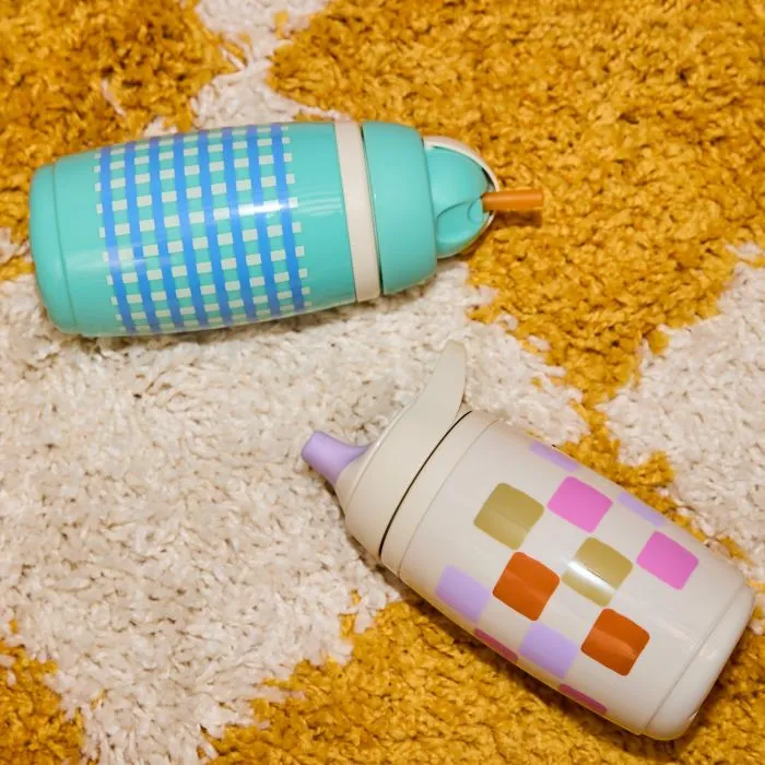 Tomme Tippee Insulated Active Spout and Straw Cups laying on a yellow and white checkerboard rug