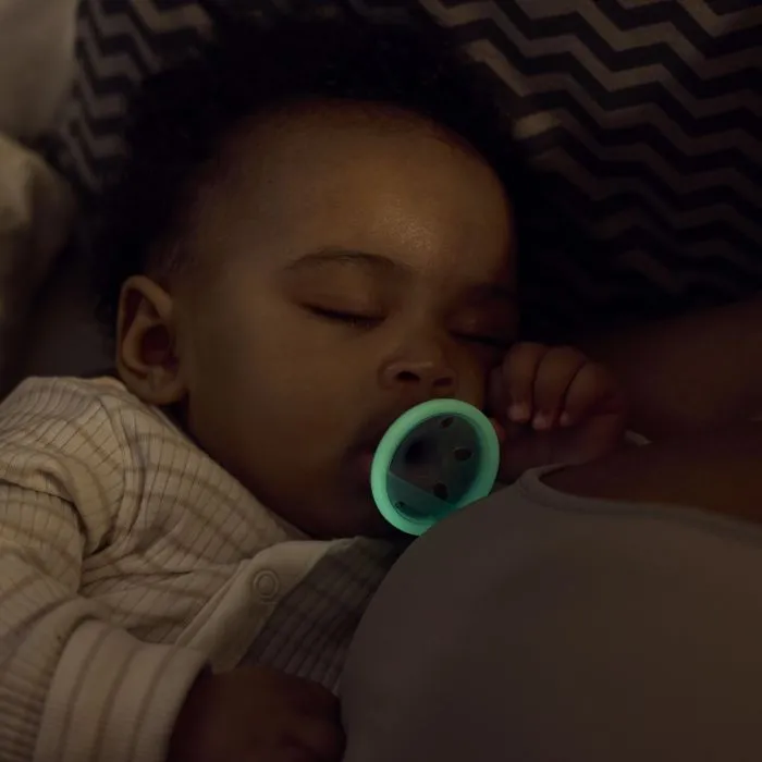 Baby with glowing soother cuddled with parent.