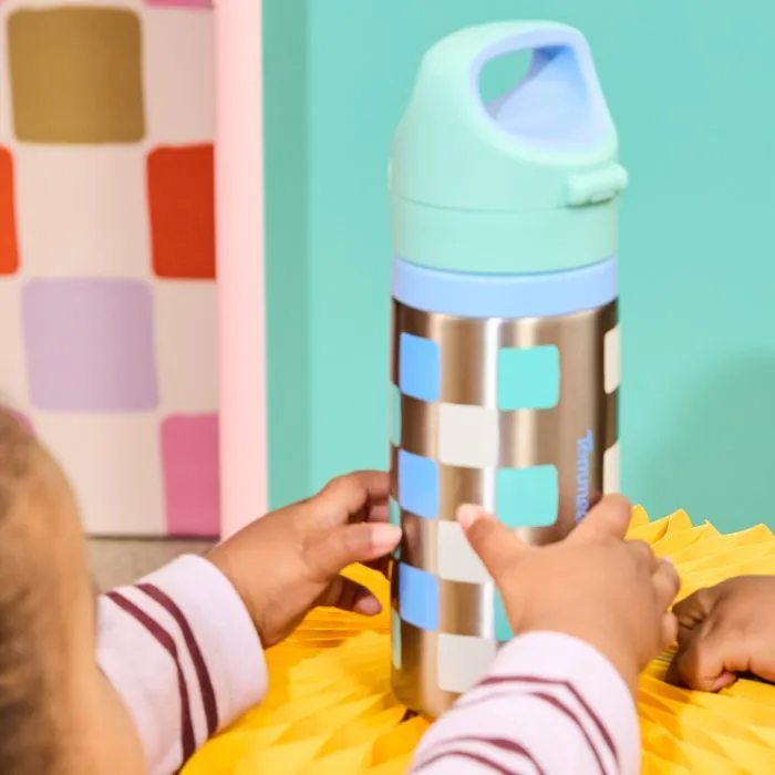 Blue Tommee Tippee On-the-Go Stainless Steel Insulated Bottle on a yellow stool with a toddler reaching out to pick it up