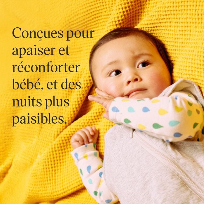 Un bébé douillet allongé sur une couverture jaune texturée, vêtu d&apos;une grenouillère à pois et d&apos;une gigoteuse gris clair.