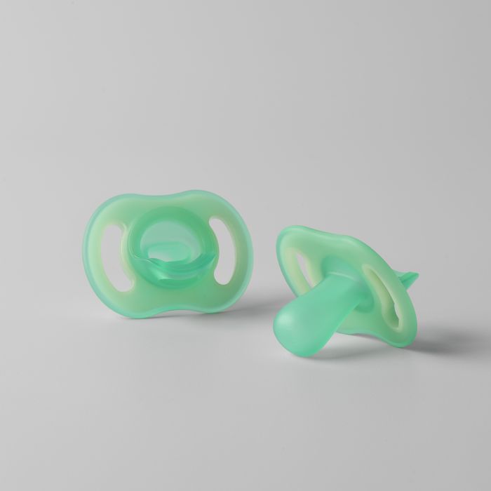 Two Night Glow soothers on a light grey background.