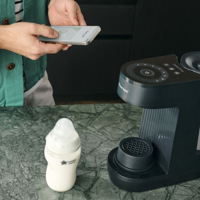 Image de la machine Perfect Prep et du biberon Natural Start sur un comptoir de cuisine avec un parent en arrière-plan utilisant l&apos;application Tommee Tippee sur son téléphone