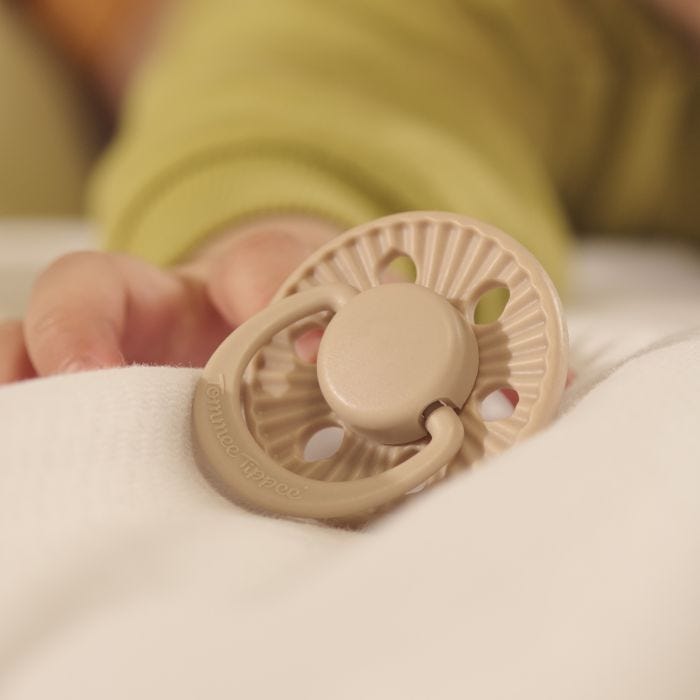 Baby reaching for a limited edition soother on bed covers.