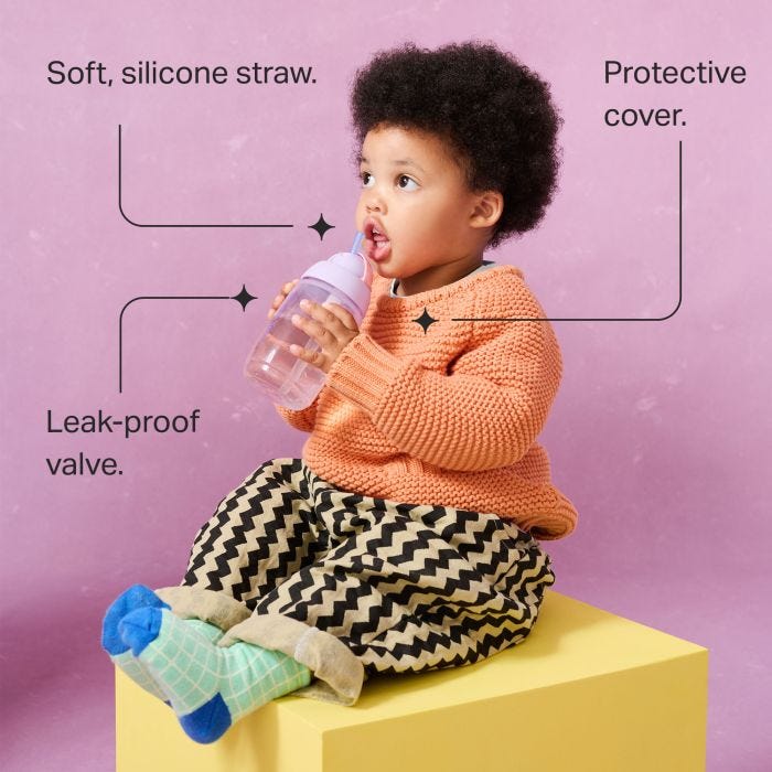Toddler sitting on a yellow box against a pink background drinking from an Active Straw cup with pointers to the key product features