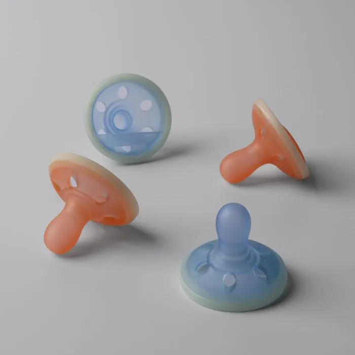 Four breast-like night glow soothers on a grey background.