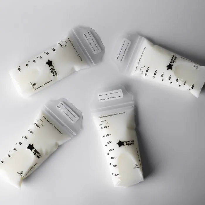 Five filled breast milk storage bags laying on a light grey background.