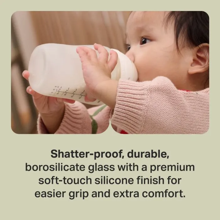 Baby drinking from a Tommee Tippee Natural Start Silicone Coated Glass Bottle with text stating "Shatter-proof, durable, borosilicate glass with a premium soft-touch silicone finish for easier grip and extra comfort"