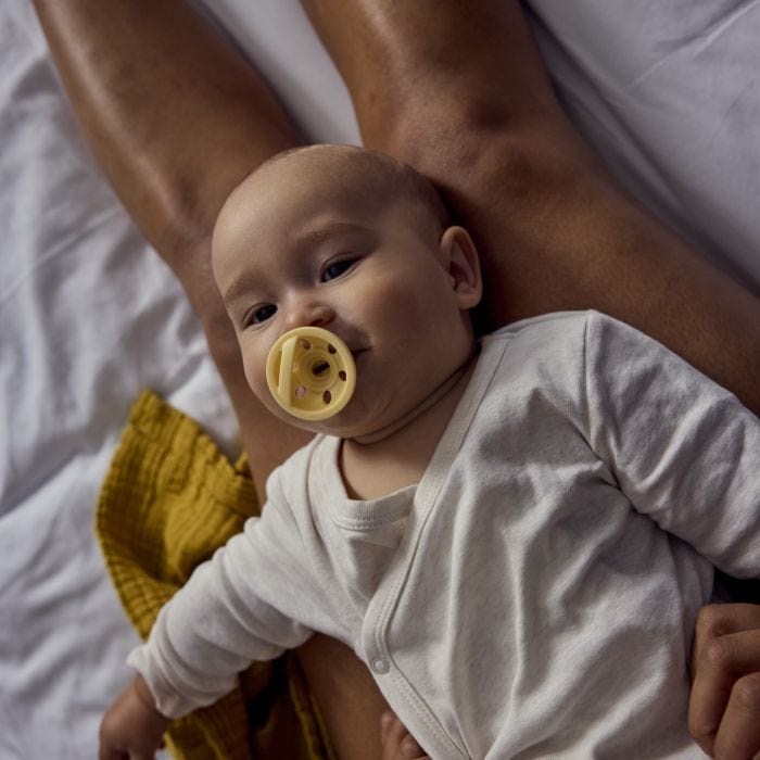 Baby laying on parent&apos;s lap with breast-like soother in their mouth.