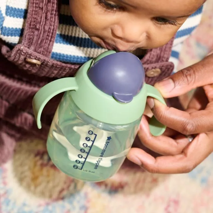 Close up of a child drinking from a green weighted straw cup