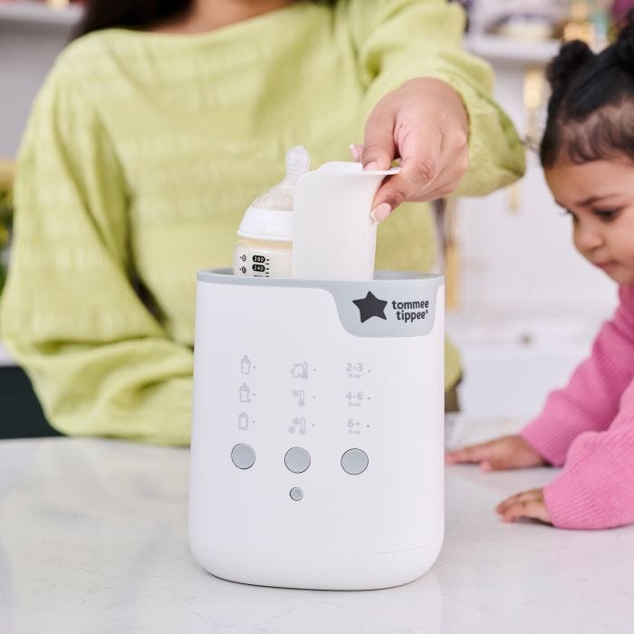 A woman using the easy-lift cradle to lower a baby bottle into a Multiwarm bottle warmer