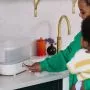 Woman holding a baby on her hip and using a steam steriliser on a kitchen worktop