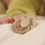 Baby reaching for a limited edition soother on bed covers.