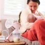 Parent feeding baby with electric breast pump containing milk.