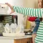 Woman holding a baby on her hip and filling a microwave steriliser ready to go in the microwave