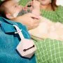 Pink soother carry case attached to bag strap with baby holding teething ring in the background.