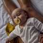 Baby laying on parent&apos;s lap with breast-like soother in their mouth.