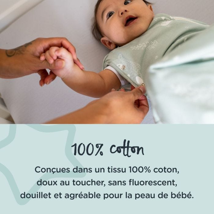 bébé couché souriant pendant que le parent ajuste le lange d&apos;emmaillotage avec un texte sur sa fabrication 100 % coton
