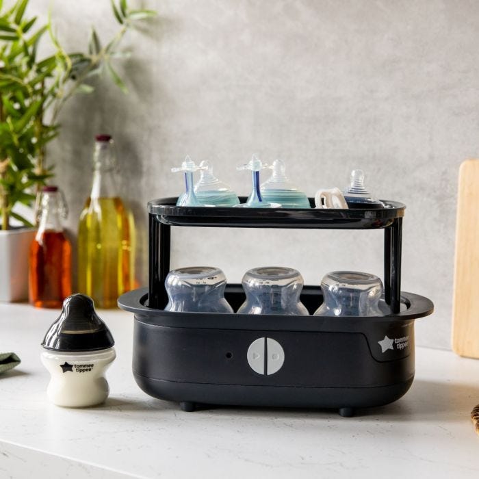 Open black steam steriliser on a kitchen counter with baby bottles inside