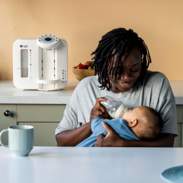Mère nourrissant son bébé dans la cuisine avec la machine Perfect Prep derrière elle