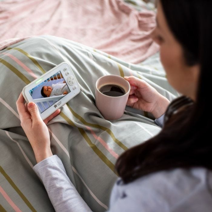 Mum in bed with a coffee watching baby on the monitor screen.