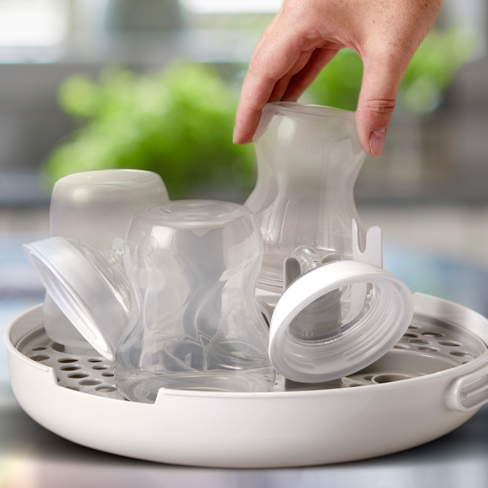 Someone placing clean baby bottles into the open microwave sterilizer