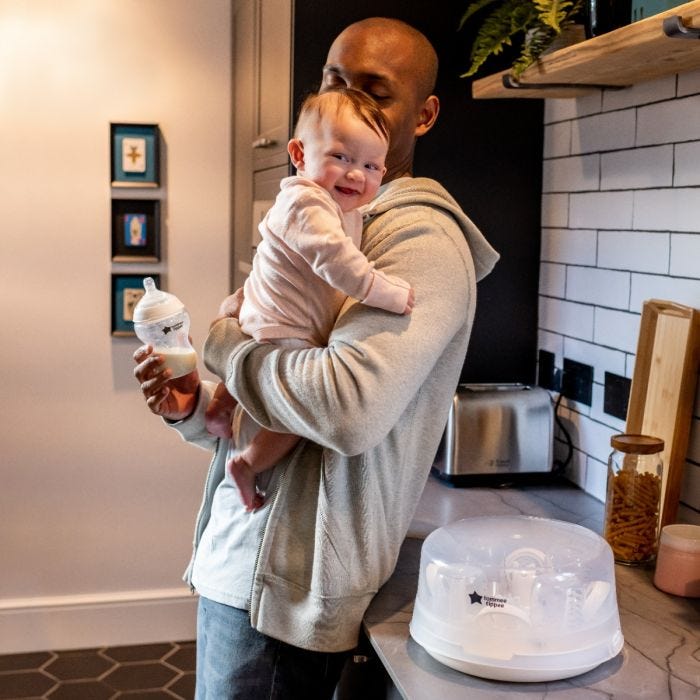 Papa avec son bébé souriant dans les bras, debout à côté de son stérilisateur micro-ondes