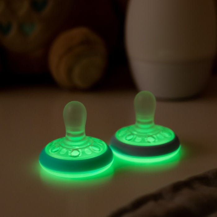 Two breast-like night soothers glowing in the dark on a white table.