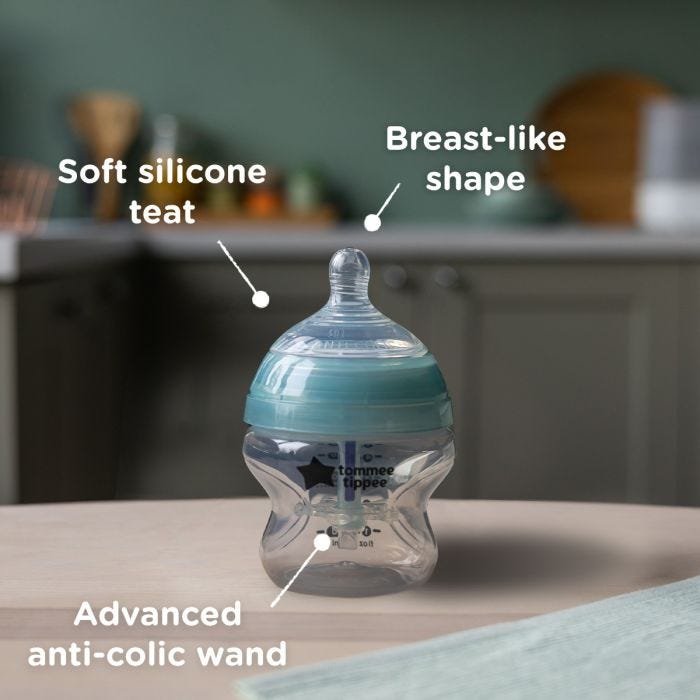 Advanced Anti-Colic baby bottle on a kitchen counter with pointers to its silicone teat, breast-like shape and anti-colic wand