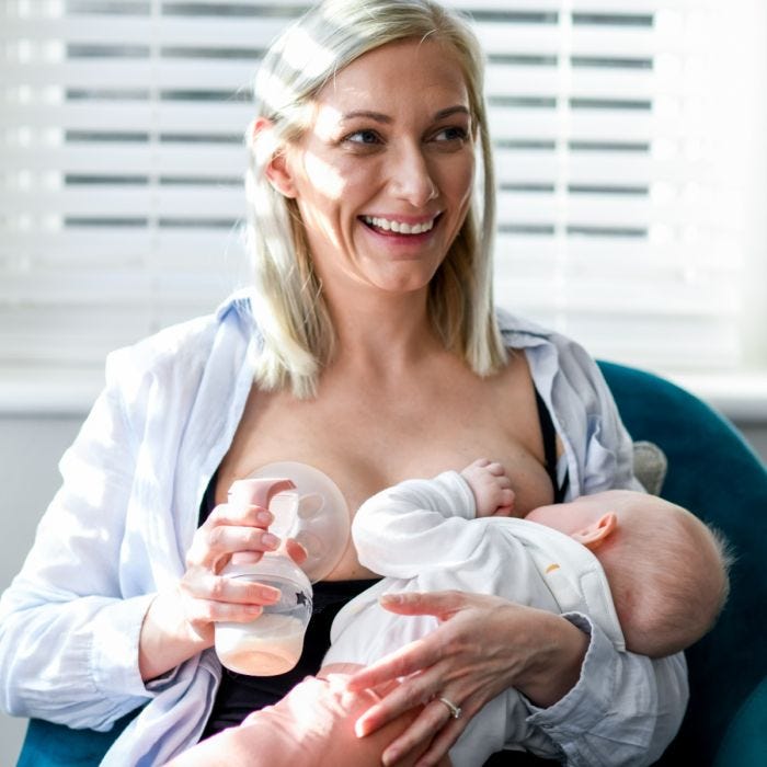 Mom breastfeeding baby and holding manual breast pump at other breast