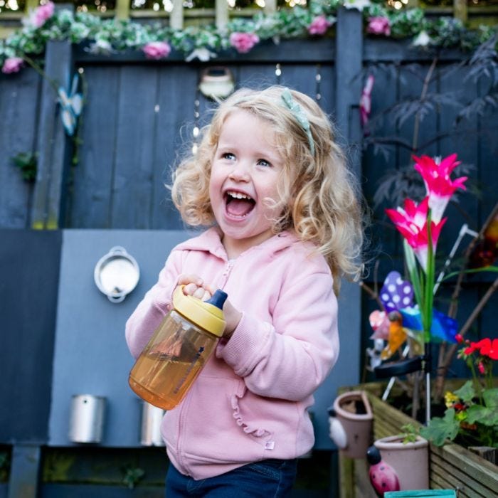 Girl with blonde hair and pink jumper laughing whilst holding the Sportee Water Bottle in Yellow