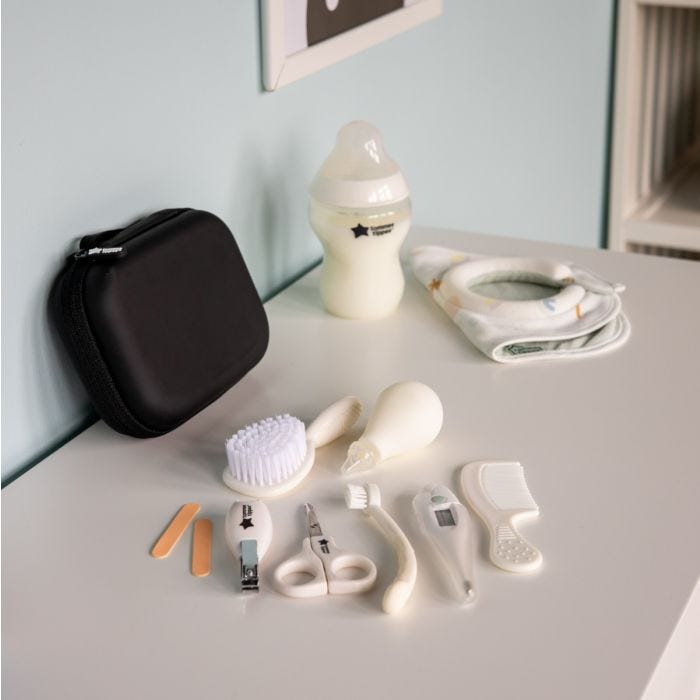 Contents of baby healthcare kit laid out on a white table next to zipped up travel case, a baby bottle and a milk feeding bib.