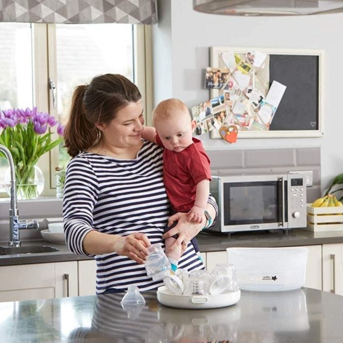 Mom holding baby and removing clean baby bottle from microwave sterilizer