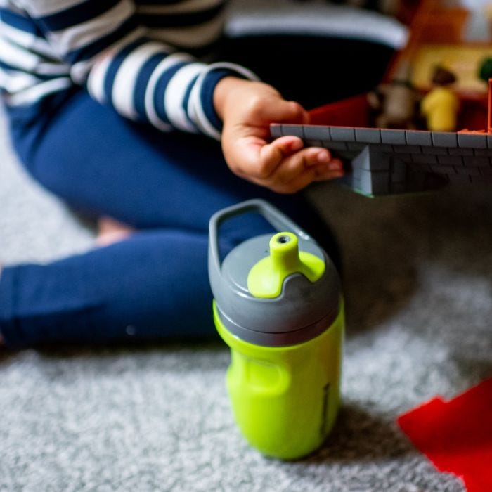 Green sportee cup on the floor next to parent reading to child