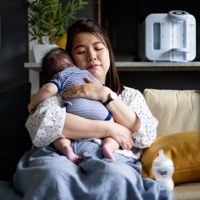 Mother holding baby alors qu&apos;il était assis sur un canapé avec une machine Perfect Prep blanc en arrière-plan
