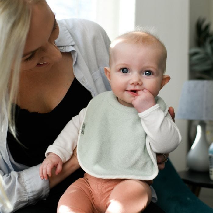 Baby wearing a green milk feeding bib sitting on mom&apos;s knee.