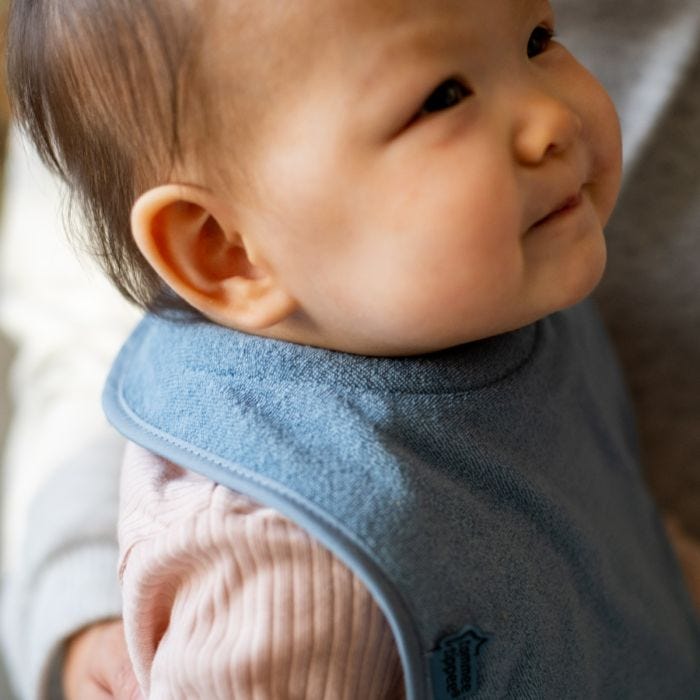Close up of baby wearing a blue milk feeding bib with padded neckband.