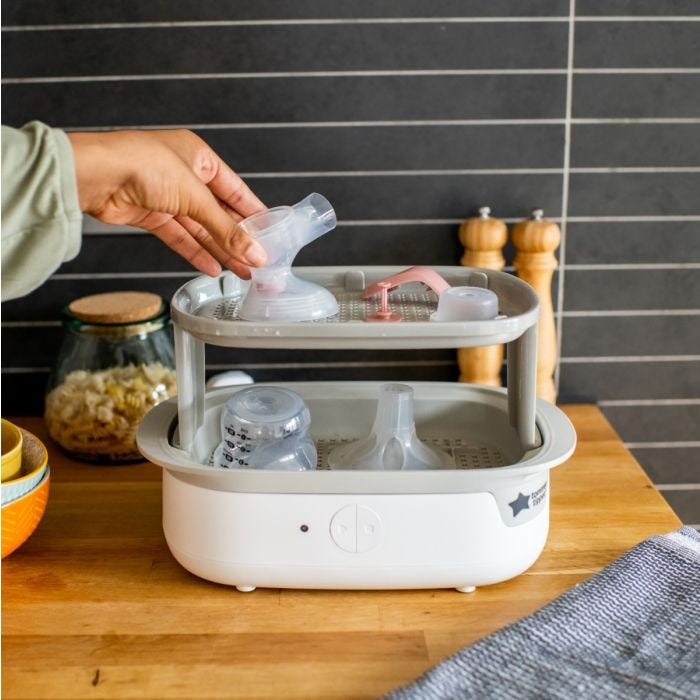 An Electric Steam Sterilizer on a kitchen counter containing each individual part of Tommee Tippee’s Manual Breast Pump.