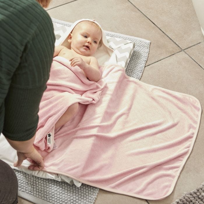 Bébé sur matelas à langer, enveloppé dans la serviette rose à capuche hug n dry.