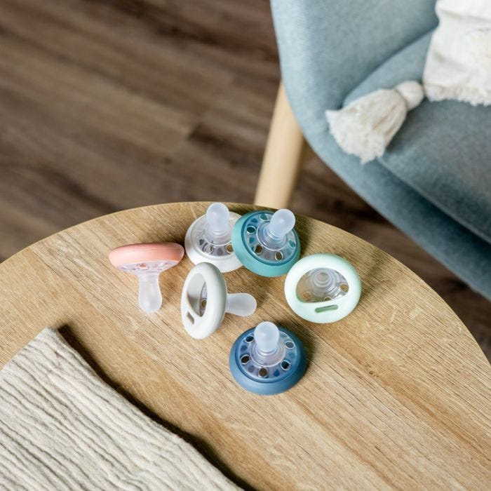 Breast-like pacifier in various colours lying on a brown table.