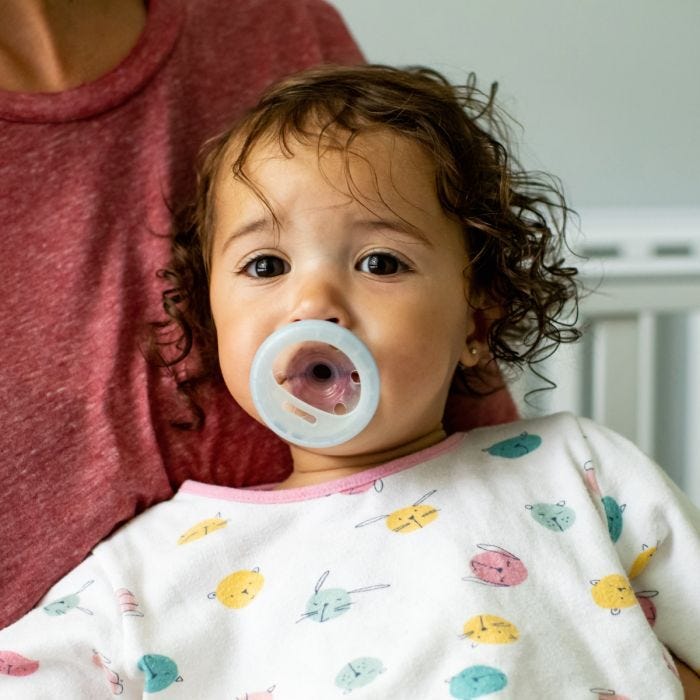 Baby girl with light blue breast-like night soother in mouth.