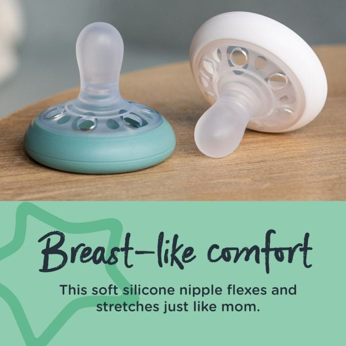 One green and one white breast-like pacifier next to each other on a brown table with text stating they offer breast-like comfort.