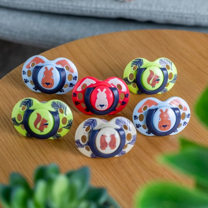 5 Fun Style soothers in various colours and designs on a brown wooden table.