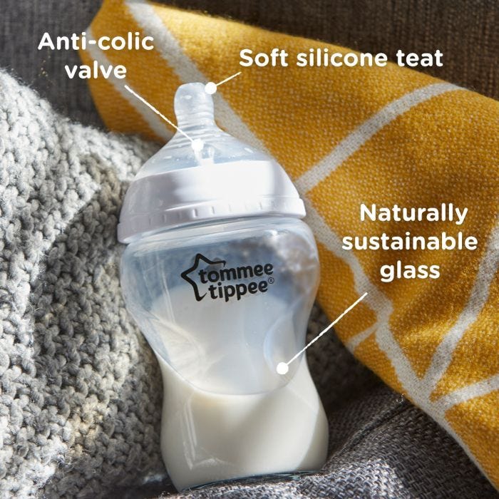 Glass baby bottle on windowsill with pointers to its silicone teat, anti-colic valve and sustainable glass base