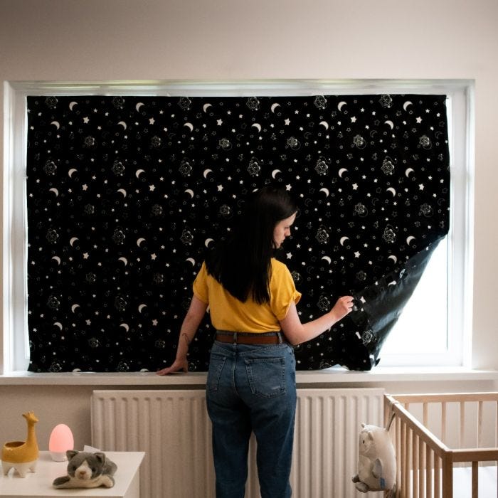 Woman in a yellow t-shirt fixing the portable blackout blind to a window in a baby&apos;s room.