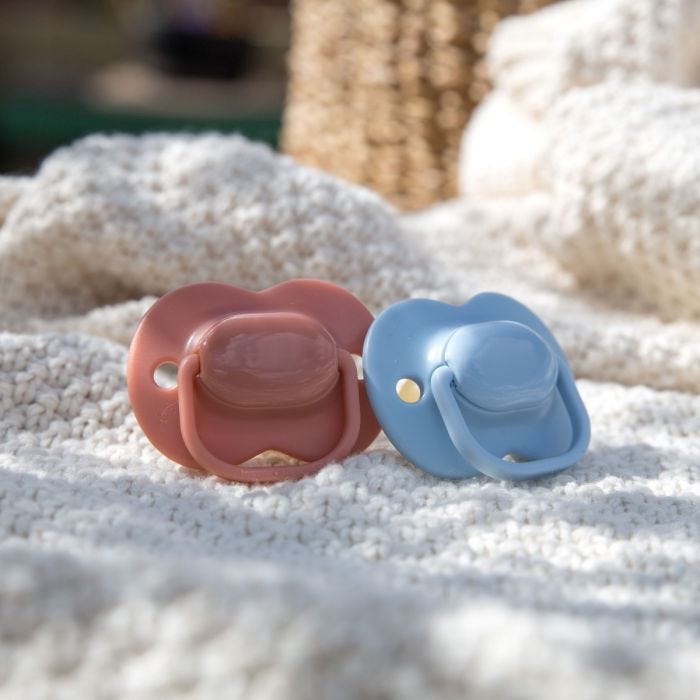 Two cherry latex soothers outside on a picnic blanket