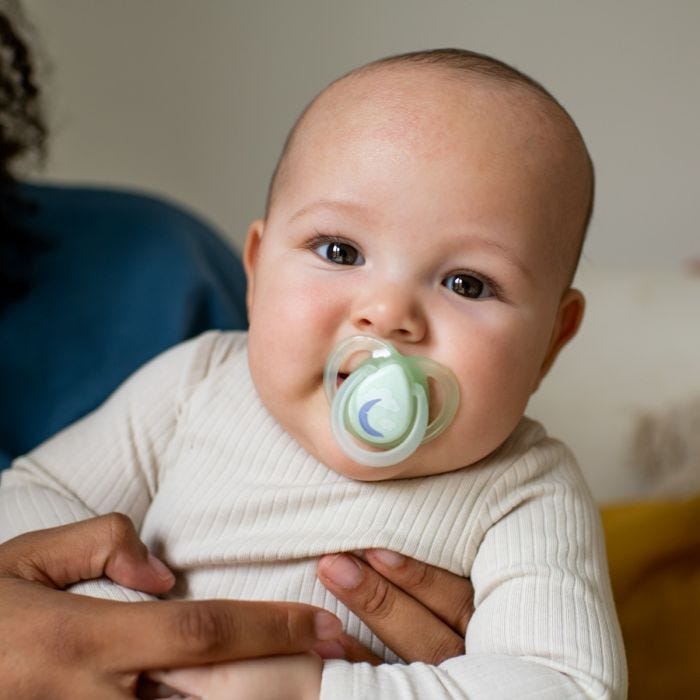Bébé tenu avec une sucette dans la bouche